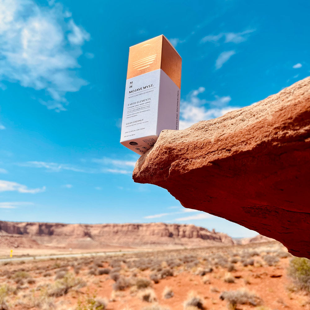 A Mojave Myst Molecular Spray Deodorant luxury box rests on the edge of a red rock cliff. In the background is red-colored desert mesas.