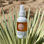A Mojave Myst Molecular Spray Deodorant spray bottle is set amongst the pointy leaves of a Yucca plant.