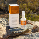 A luxury box of Mojave Myst with spray bottle next to it on a rock near a desert Creosote bush.