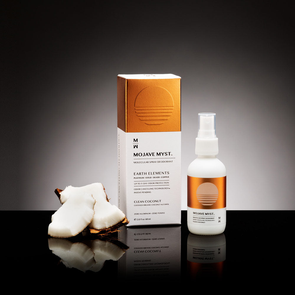 
                  
                    A luxury box of Mojave Myst Molecular Spray Deodorant with a spray bottle next to it on a black reflective surface. There are pieces of coconut next to the box.
                  
                