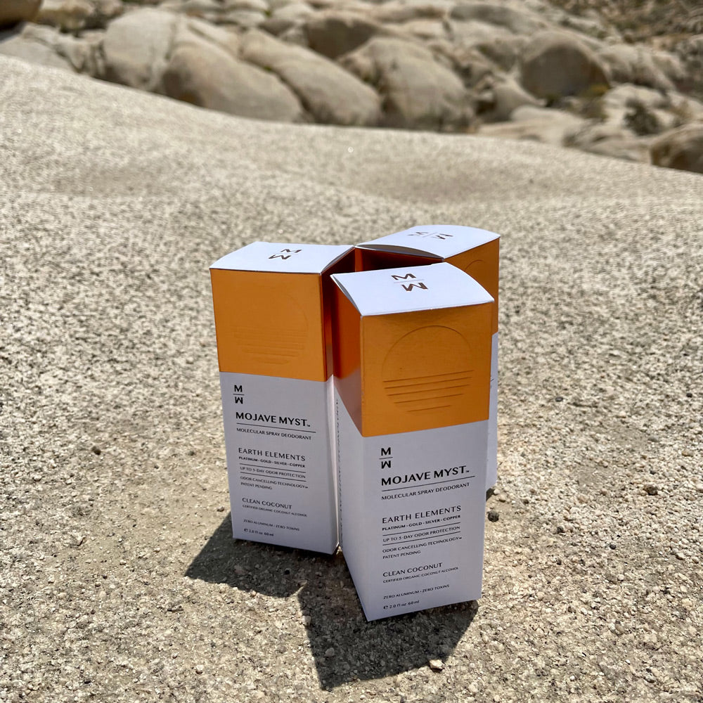 
                  
                    Three luxury boxes of Mojave Myst Molecular Spray Deodorant resting on a large, granite rock.
                  
                